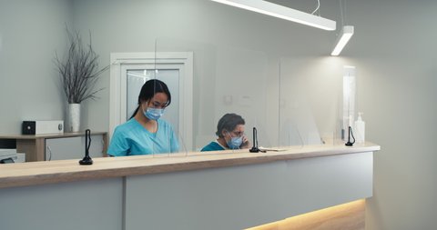 Zoom in view of Asian woman giving directions to man with broken arm while working on reception of modern clinic near doctor