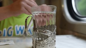 Closeup view video footage of cute white kid passenger making and drinking hot tea from transparent glass standing in metal holder while travelling by train in Ukraine