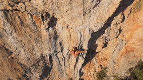 aerial view from drone of strong muscular young man climbs on crag with big tufa by challenging rock climbing route. climber resting by hanging on hand, chalking hand and make effort on handhold. 