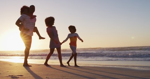 African american family having fun walking together during sunset on the beach. family travel vacation leisure concept