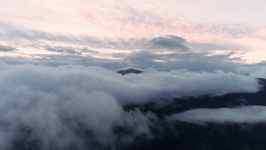 Amazing clouds of dense fog move flowing over mountain Sunrise or sunset sky fog scenic aerial view. Dark sunrise aerial view of Carpathian Mountains in Ukraine. Dark mounts in mist. Above clouds.