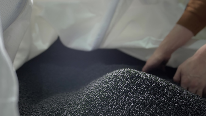 Hands lift black polymer granules from a cloth bag in a garbage recycling plant. Plastic pellets are crumbling or poured from the palms. Raw materials for recycled plastic are used in manufacturing. | Shutterstock HD Video #1071557506
