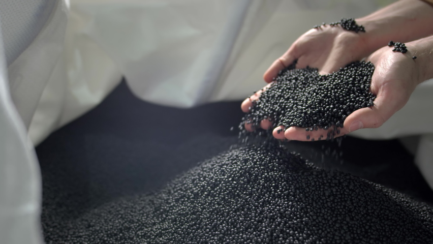 Hands lift black polymer granules from a cloth bag in a garbage recycling plant. Plastic pellets are crumbling or poured from the palms. Raw materials for recycled plastic are used in manufacturing. | Shutterstock HD Video #1071557506
