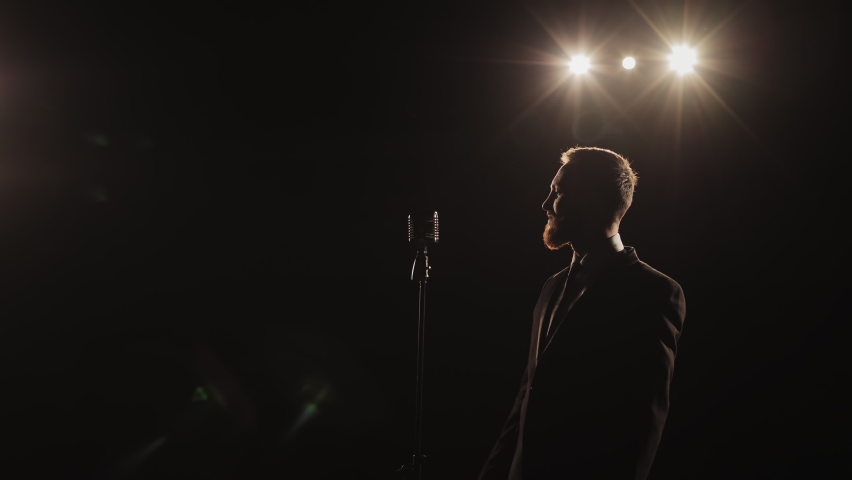 The man is holding the microphone and singing. He is leaning back and the spotlight shining on him. 4K