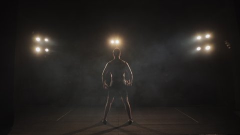 A man is dressing in tights is standing on the stage. He is raising the winner's Cup and waving it. The spotlight is shining on him. Shooting from behind. 4K