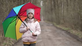 Portrait of a girl with an umbrella in the park. A child walks in rainy weather on a trail in a landscape park. Lifestyle video of a teenager's life.