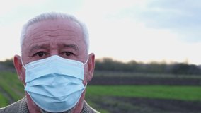 An elderly man in a medical mask looks at the camera. Close up portrait of a senior
