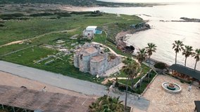 Ancient Orthodox church located on the cliff next to the sea. Agios Philon church in Karpasia, North Cyprus.  Aerial drone video of chapel is surrounded by blue water sea and palm trees.