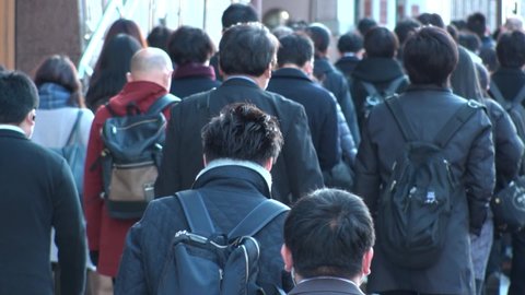 TOKYO, JAPAN - MAR 2020 : Back shot of crowd of people walking down the street in busy morning rush hour. Many commuters going to work. Japanese business, job and lifestyle concept. Slow motion shot.