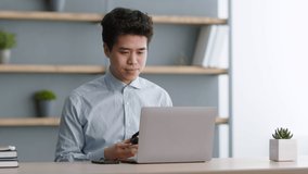 Online meeting. Young asian office worker putting on headset and video chatting with colleagues, discussing business plans, sitting at workplace, slow motion