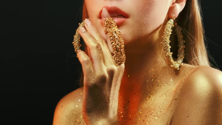 beauty fashion model girl's mouth close-up. Golden body skin. Glamour golden bright color. gold metal hand, finger touches juicy lips. Beautiful artistic makeup shiny paint on woman face. Lady goddess Royalty-Free Stock Footage #1071574864
