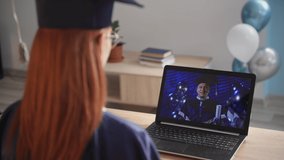 female student in academic mantle at remote graduation via laptop video link during remote education, close-up