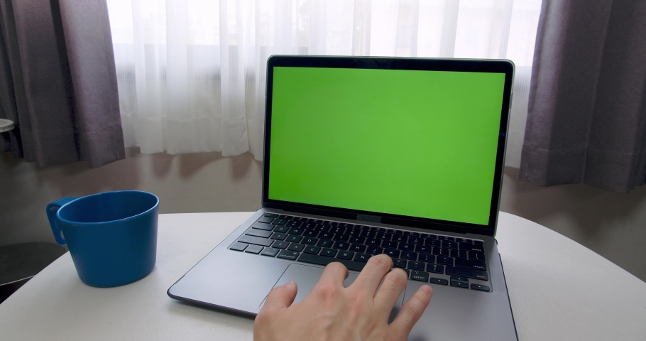 Man hand using trackpad (touchpad) to use laptop computer with Green Screen chroma key. There is a blue plastic mug on the table. Simple, develop, stylish remote work concept Royalty-Free Stock Footage #1071583426