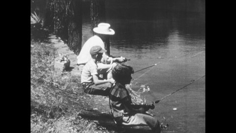 1940s: Boy puts down fishing pole and walks away from lake. Man and girl fishing. Boy points at ground and shouts. Man picks up snake.