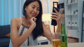 Young Asia lady drinking beer having fun happy moment night party New Year event online celebration via video call by phone at home at night. Social distancing, quarantine for coronavirus prevention.