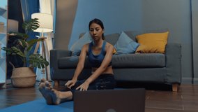 Young Asia lady in sportswear exercises doing work out and using laptop to watch yoga video tutorial at home night. Distant training with personal trainer, social distance, online education concept.