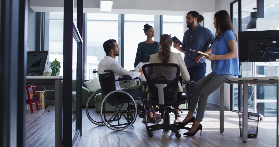 Diverse group of work colleagues talking at casual office meeting, one in wheelchair. independent creative business in a modern office.
