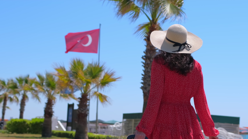 Traveler woman traveling in red dress, hat walking with suitcase at luxury resort on background flag of Turkey blue sky. Female tourist woman in hotel. travel tourism beach vacation happy holiday Royalty-Free Stock Footage #1071601192