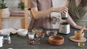 Midsection PAN shot of two unrecognizable women standing by wooden table making diy scrub, using blender for grinding aromatic coffee beans - Powered by Shutterstock - Get 15% off with code: PIKWIZARD15