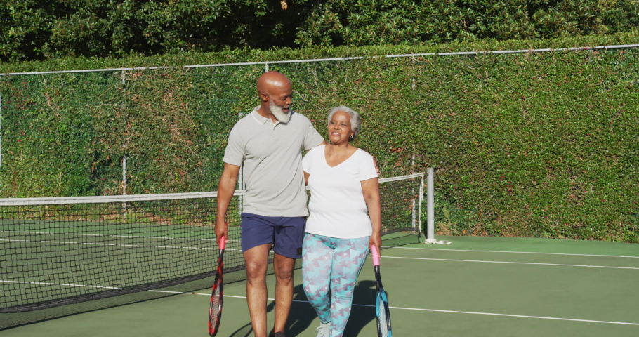 African american senior couple holding rackets walking on the tennis court. retirement sports and active senior lifestyle. | Shutterstock HD Video #1071603835