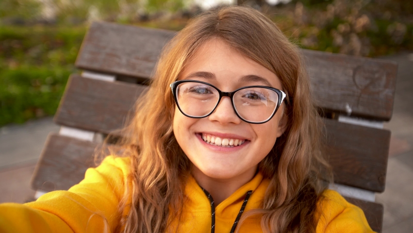 Pretty teen girl in glasses making video call with friends in quarantine. Smiled young girl blogger recording vlog in social media,live streaming,looking to smartphone screen on in park.Making selfie | Shutterstock HD Video #1071604915