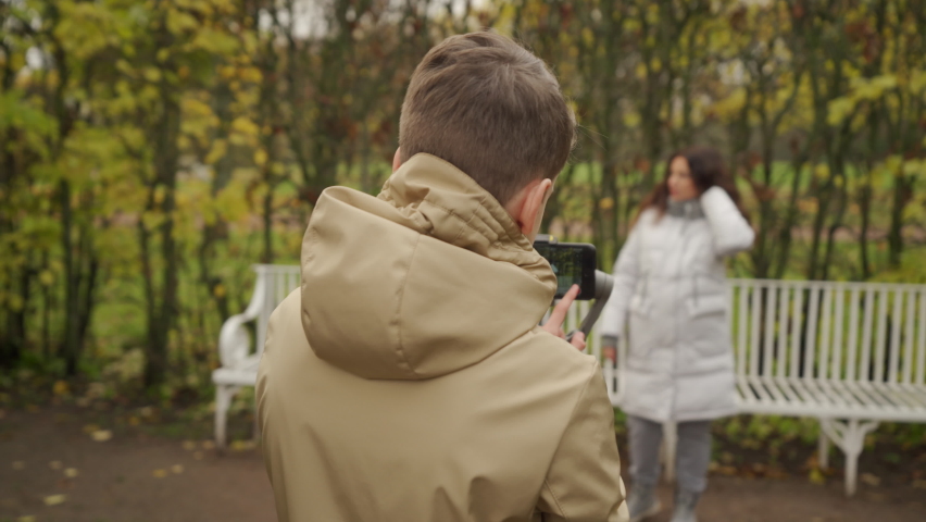 Mother with son walk in autumn park boy with mobile phone camera recording outdoor video blog. Teenager shooting video for travel vlogging. Catherine Park, Tsarskoye Selo, Saint Petersburg, Russia.