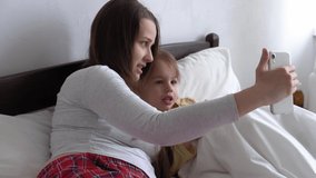 caucasian family little children girl and young woman mom talking in video conference by smartphone together at home with happiness smile on white bed. technology, lifestyle, mobile phone use concept