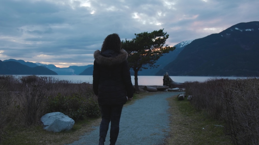 Adventurous Adult Woman Walking on a Trail in the park. Pacific Ocean Coast with Canadian Mountain Landscape. Sunset Sky. Howe Sound between Squamish and Vancouver, British Columbia, Canada.