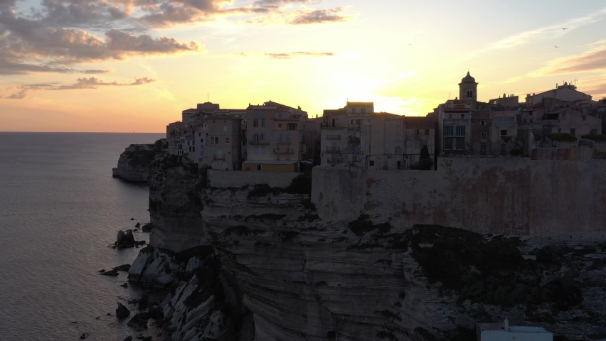 France, Corse, Bonifacio, drone aerial view during the sunset (or sunrise) above the cliffs with a big gold sun behind the church of the old town Royalty-Free Stock Footage #1071609403