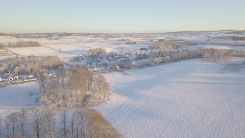 Amazing winter landscape with trees and fields covered with white snow till the horizon on a bright cold day in Scotland during golden hour. Drone trucking shot