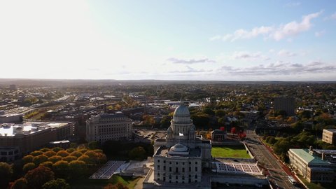 Providence, RI - October 21st, 2020: The flag flaps in the wind on top of the historic Rhode Island State House with its large dome and white masonry exterior surrounded by autumn colored trees.
