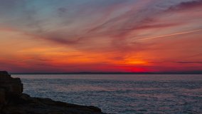 Late evening stunning sky after sunset lights up red on fire, like a mythical flaming phoenix. Rocky cliff coast silhouette. skyline lighting up on the other coast timelapse video. Bristol channel 