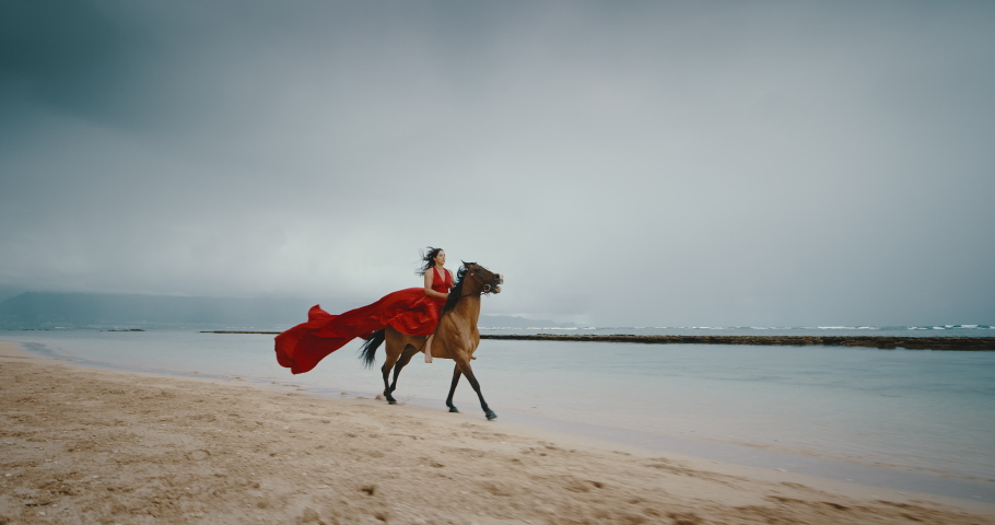 Beautiful woman horseback riding on the beach in flowing red dress, cinematic slow motion Royalty-Free Stock Footage #1071622552