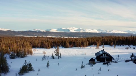 Winter nature in Sweden. Mountains snowy snow covered and forest in sunset evening light. wild natural environment with single small house. light and sunny skies in aerial drone shot