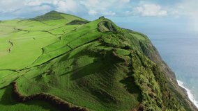 Drone flying over green mountains of Sao Jorge island in atlantic ocean, Azores, Portugal, Europe. Overhead view of summer scene with green farm meadows covering island area, 4k footage
