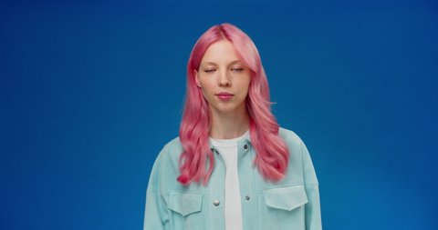 Young woman with pink hair considering serious plan, solving problem in mind and nodding approvingly, thinking over smart idea, pondering and musing answer. Studio shot isolated on blue background