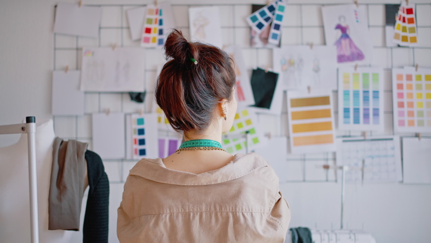 Creative process. Back view of young fashion designer looking at inspiration board at workshop and pondering about new clothes collection, zoom out shot | Shutterstock HD Video #1071624469