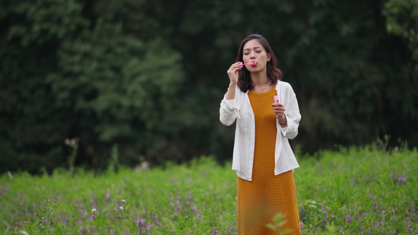 beautiful asian girl enjoy relax in the nature park blowing soap bubble in the morning blooming field