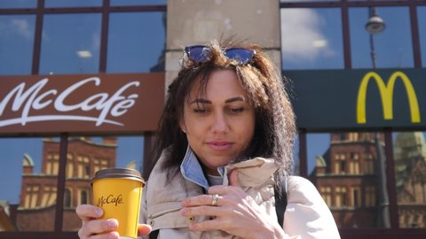 WROCLAW, POLAND - APRIL 27, 2021: A Brunette Woman with Yellow McCafe Cup of Coffee in front of McDonald's Fast Food Restaurant