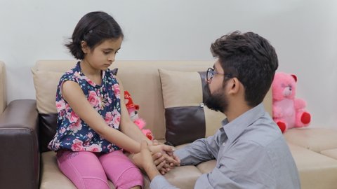Indian father making his upset child comfortable - childhood sad moments. The angry daughter sitting on a sofa while her dad consoling her - Indian parenting