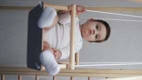 Cute little boy is riding on swing rope at home, happy baby smilling , vertical video side view