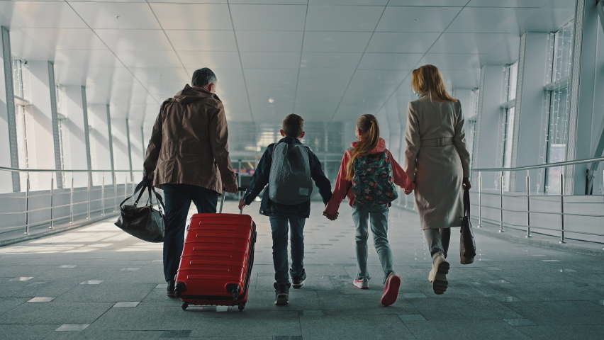 Family of two parents and two kids with luggage walking down the airport terminal, all wearing protective masks, back view, slow motion Royalty-Free Stock Footage #1071644425