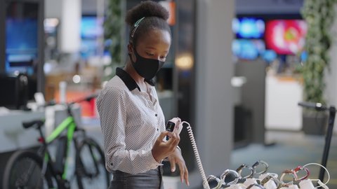 young afro-american shopper woman is choosing smartwatch in digital equipment store, viewing models on demonstration showcase