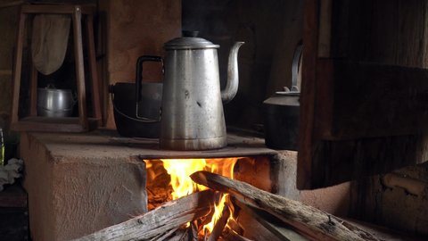 Close up of metal teapot heating water to make organic coffee on the fire in a rustic wood stove. Minas Gerais, Brazil. Concept of, winter, cold, cozy, vintage, morning, coffeemaker, retro. 4K