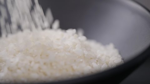 Japanese rice falling in slow motion. Close-up raw rice grain in black bowl