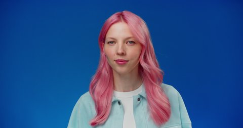Young woman with pink hair considering serious plan, solving problem in mind and nodding approvingly, thinking over smart idea, pondering and musing answer. Studio shot isolated on blue background