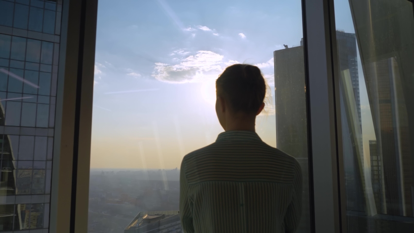 Success, opportunity, sightseeing, discover, corporate, future concept. Back view of pensive woman silhouette looking at cityscape through window of skyscraper. Summer time, sun lens flare, daylight | Shutterstock HD Video #1071655942