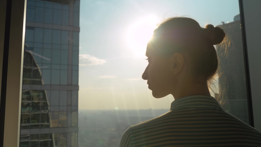 Back view of woman silhouette looking at cityscape through window of skyscraper. Summer time, sunset, sun lens flare. Success, opportunity, sightseeing, discover and future concept | Shutterstock HD Video #1071655945