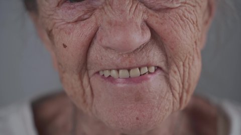 Close-up contented caucasian senior woman looking at camera smiling and laughing over gray background. Portrait of a grandmother 90 years old happy in the studio. Denture for an elderly person