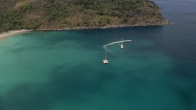 White yacht and catamaran anchored in blue water near a paradise tropical island. Self-isolation on boat. Travel business is recovering from the coronavirus pandemic. Drone video top bird eye view.